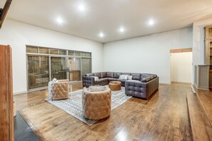 A spacious living room with a large sectional sofa, two ottomans, and a glass sliding door leading to a balcony.