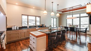 A modern kitchen with a central island, bar stools, and large windows offering a view of a snowy landscape.