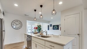 Une cuisine moderne dotée d’un grand îlot central, d’appareils électroménagers en acier inoxydable, de luminaires suspendus et offrant une vue sur la salle à manger.