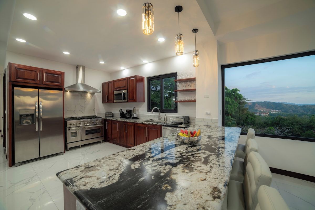 A modern kitchen with a large island, stainless steel appliances, and a view of the landscape.