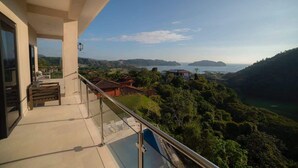 Un balcón con vista a un paisaje costero, que incluye colinas y una masa de agua.