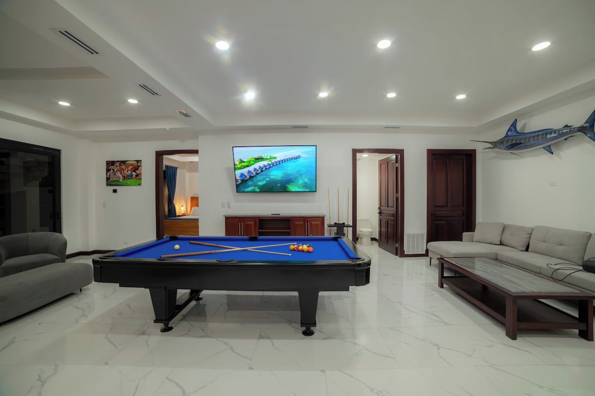 A modern living room with a pool table, a sofa, a television, and a decorative fish mounted on the wall.