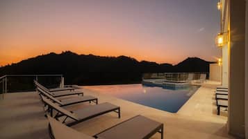 A rooftop pool area with lounge chairs and a view of a mountain at sunset.