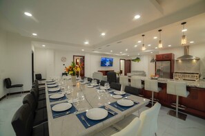 Un comedor moderno con una mesa larga dispuesta para una comida, una cocina con estufa y un televisor montado en la pared.