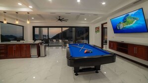Un moderno salón con una mesa de billar, un televisor grande y vistas al exterior.