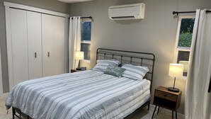 A bedroom with a bed, nightstands, a window with curtains, an air conditioning unit, and a wardrobe. - Bremerton Retreat-30 min Fast Ferry to Seattle-Pet Friendly (Bremerton)