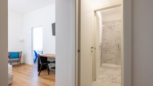 Un intérieur moderne avec un plancher en bois, un coin repas comprenant une table et des chaises, et une salle de bain dotée d’une douche en marbre.