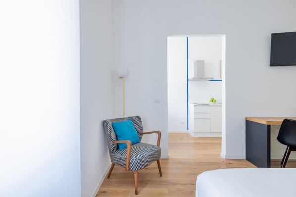 A modern, minimalistic room with a wooden floor, a bed, a desk, and a chair.