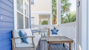 Une terrasse en bois avec une balustrade blanche, un canapé avec des coussins et une décoration en forme d’étoile de mer.