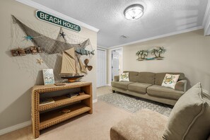 A living room with a beach-themed decor, including a sign that reads "BEACH HOUSE," a net with starfish, and a ship model on a console table. - Cotton Bayou 8C | Waterfront | Boat Slip & Launch | Pool | Beach Getaways (Orange Beach)