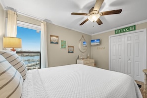 A bedroom with a bed, a ceiling fan, a TV, a dresser, and a view of the water. - Cotton Bayou 8C | Waterfront | Boat Slip & Launch | Pool | Beach Getaways (Orange Beach)