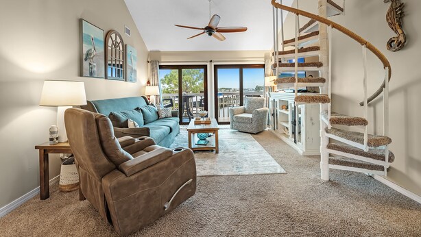 Ein geräumiges Wohnzimmer mit einem braunen Ledersofa, einem blauen Sessel, einem Holztisch und einer weißen Wendeltreppe.