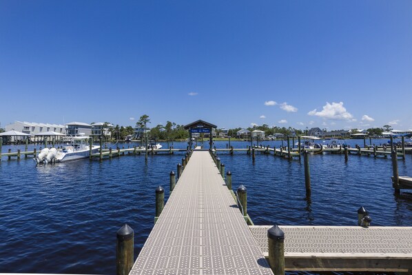 A pier leading to a dock with boats, a building with a sign, and a clear blue sky. - Cotton Bayou 8C | Waterfront | Boat Slip & Launch | Pool | Beach Getaways (Orange Beach)