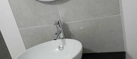 Ein Badezimmer mit einem weißen Waschbecken, einem runden Spiegel und grauen Fliesen.