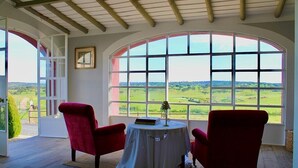 A room with a large arched window, two red chairs, a small round table with a lamp, and a framed picture on the wall. - Villa HERDADE DA BOAVISTA: 1.000 sqm house just for YOU! Capacity: 20 guests. (Aljustrel)