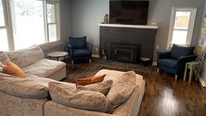 Una sala de estar con chimenea, dos sillones, un sofá y un televisor.