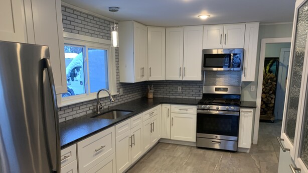 Una cocina moderna con armarios blancos, electrodomésticos de acero inoxidable, una encimera negra y una ventana con vistas a la nieve.