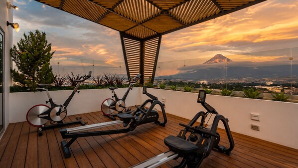 A rooftop gym with exercise equipment and a view of a mountain.