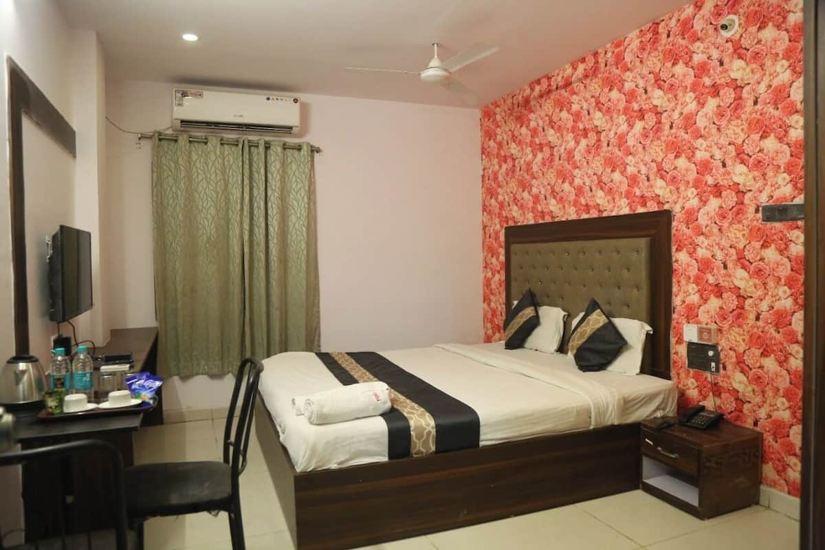 A hotel room with a bed, a desk, a chair, a TV, an air conditioner, a ceiling fan, and a floral wallpaper.