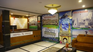A hotel lobby with a reception desk, a chandelier, a sofa, and posters of landmarks. - Hotel MN Grand (Hyderabad)