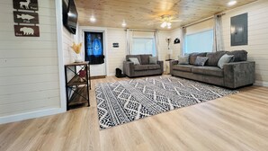 A cozy living room with a wooden ceiling, two grey sofas, a patterned rug, and wall-mounted decorations.