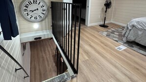 A room with a wooden ceiling, a clock on the wall, a bed, and a fan.