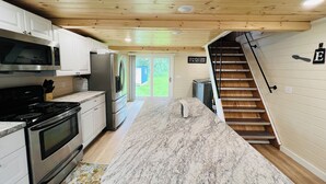 A modern kitchen with a marble countertop, stainless steel appliances, and a wooden ceiling.