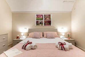 A neatly made bed with pink bedding, two bedside tables with lamps, a framed picture above the bed, and a book on the bed.