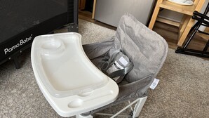 Un baño químico con asiento blanco y una bolsa gris para guardar, sujeto a una estructura de metal.