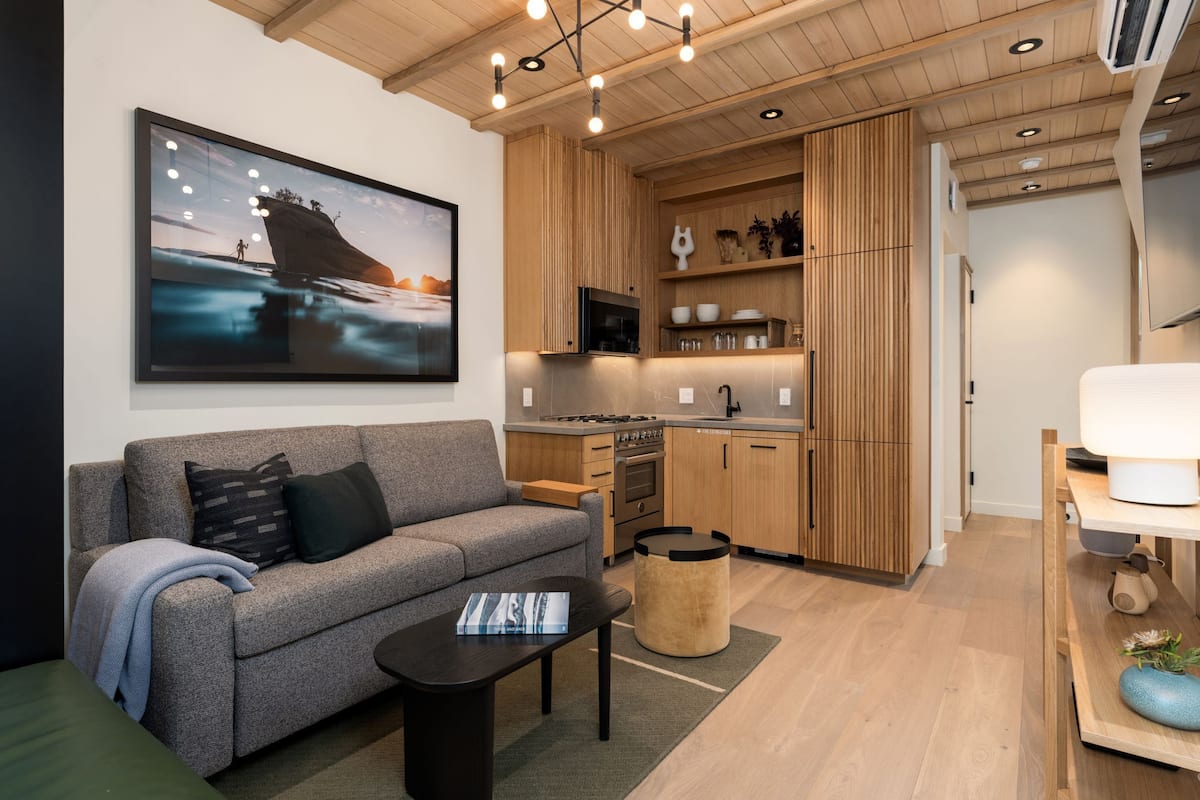 A modern living room with a grey sofa, a black coffee table, and a large painting of a ship on the wall.
