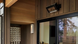 A modern spa area with a hot tub, wooden flooring, a seating area, and a glass door leading to an outdoor space.