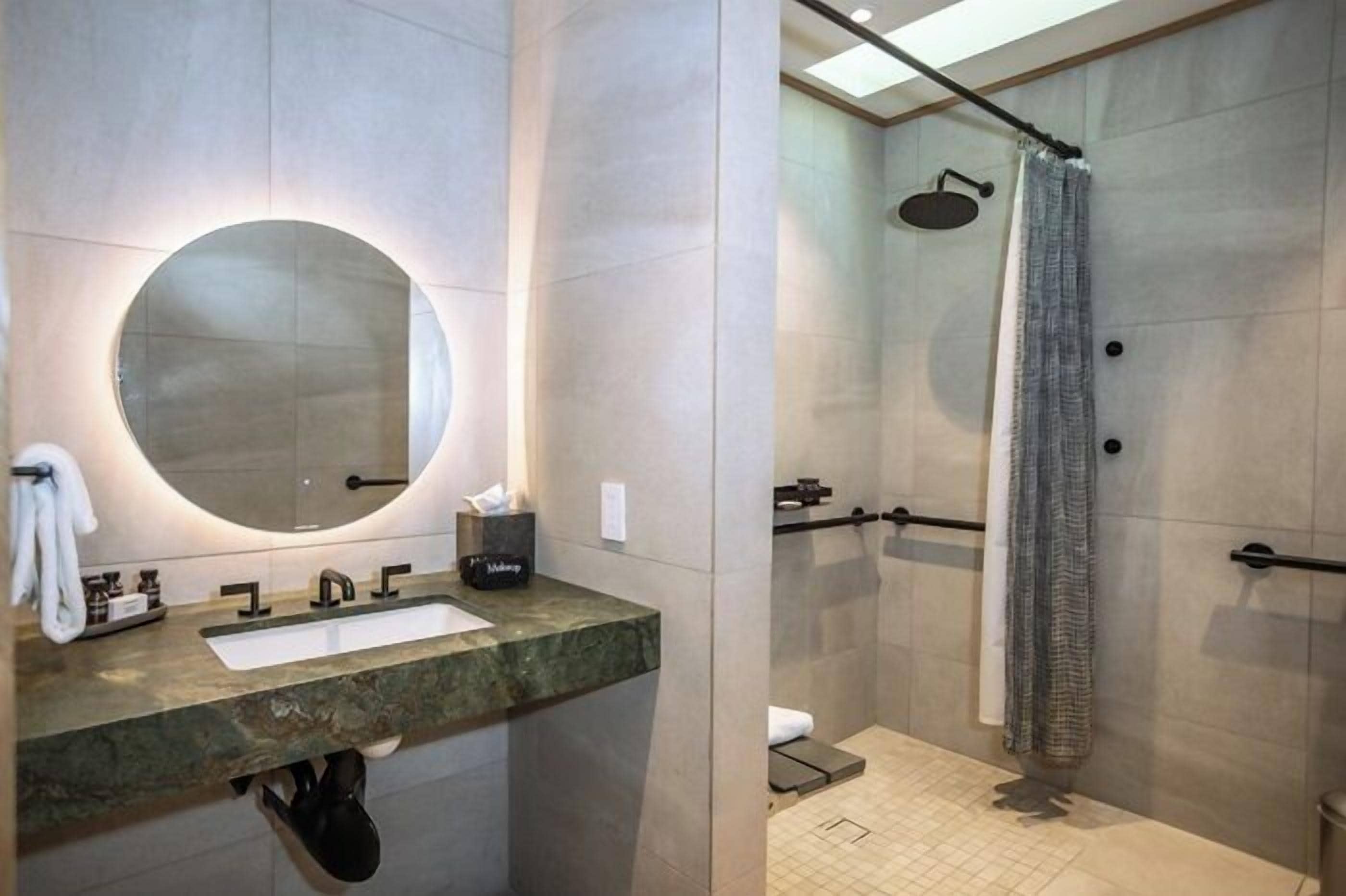 A modern bathroom with a round mirror, a sink, and a shower area with a curtain.
