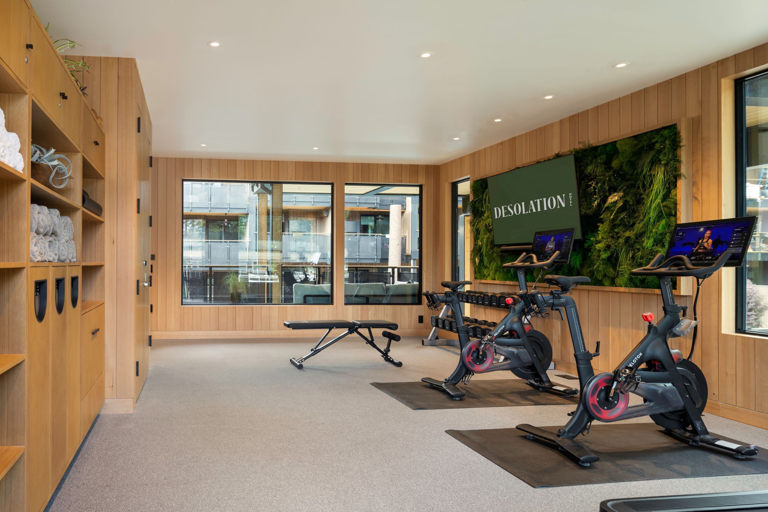 A gym with exercise bikes, a bench, and a wall-mounted screen displaying "DESOLATION".