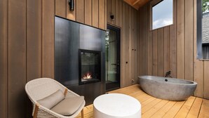 A modern outdoor area with a fireplace, a large bathtub, and a wicker chair.
