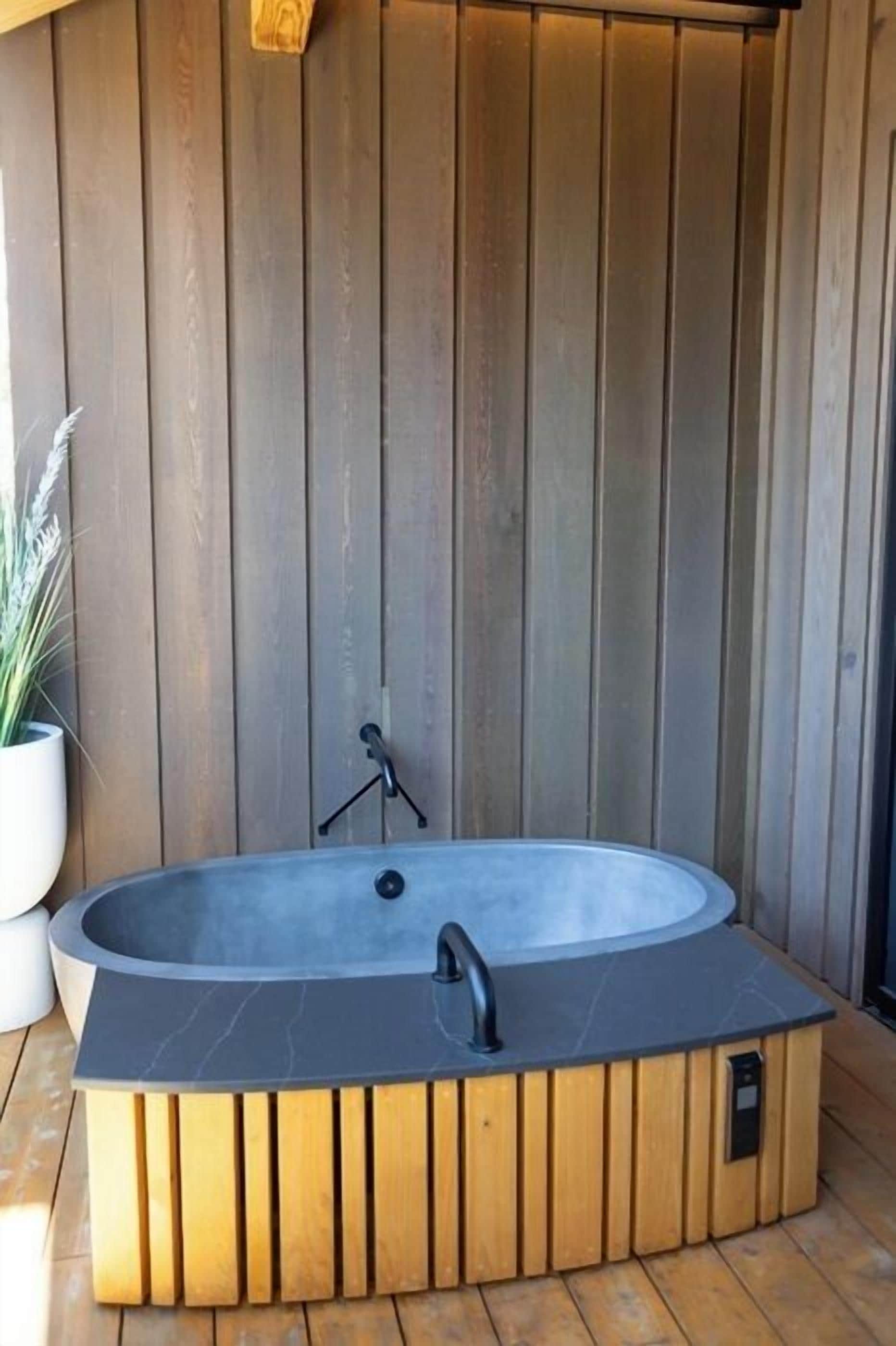 A wooden spa tub with a black faucet and control panel, set against a wooden wall.