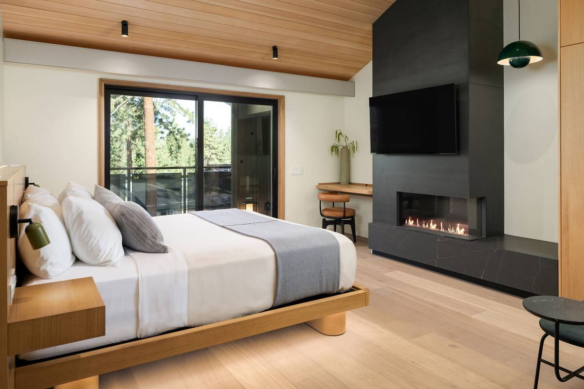 A modern bedroom with a bed, a fireplace, a TV, and a large window.