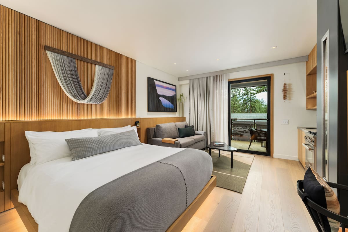 A modern hotel room with a large bed, a sofa, a dining area, and a view of the outdoors.