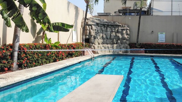 A swimming pool with clear blue water, surrounded by a stone wall and palm trees. - Hostel Nucapacha (Guayaquil)