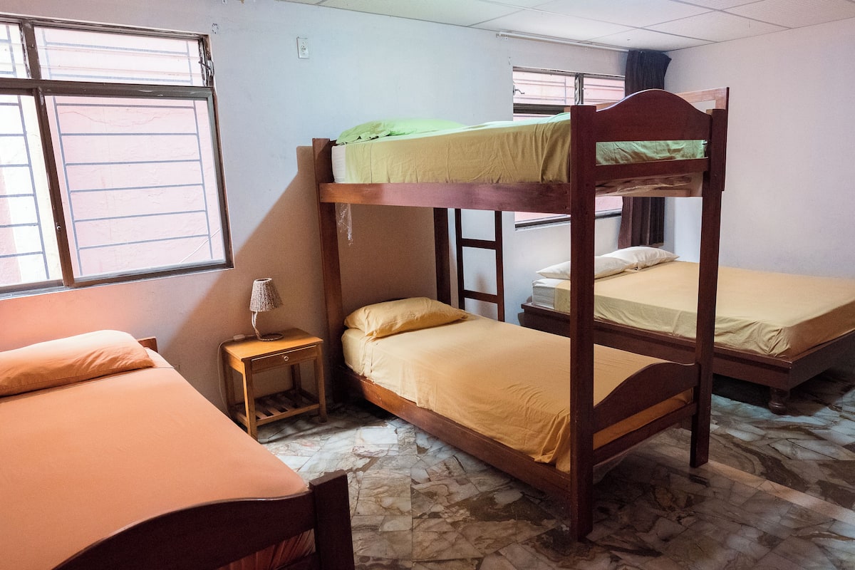 A dormitory room with bunk beds, a small bedside table, and a window with bars.