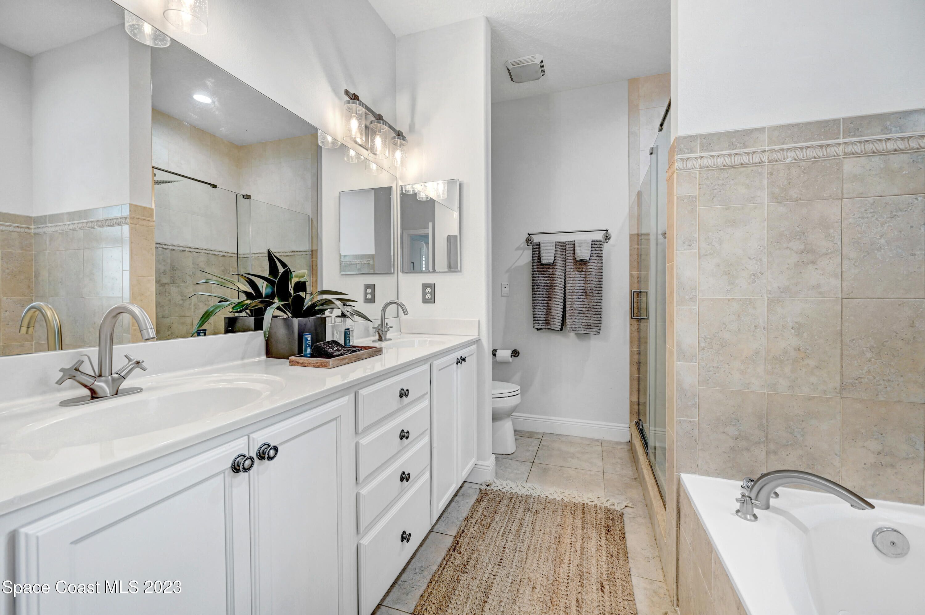 A modern bathroom with dual sinks, a large mirror, a shower, and a bathtub.