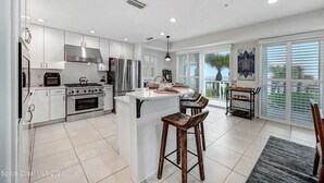 A modern kitchen with white cabinets, stainless steel appliances, and a large island with bar stools. - Luxury Oceanfront Beach House - all bedrooms have spectacular views - Sleeps 6+ (Melbourne Beach)