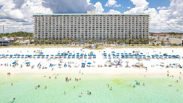 Ein großes Hotel mit Strand vor der Tür, zahlreichen Sonnenschirmen und Menschen, die den Strand genießen.