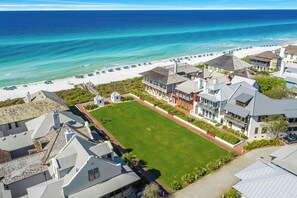 An aerial view of a coastal property with a large lawn, beachfront, and multiple buildings with balconies.