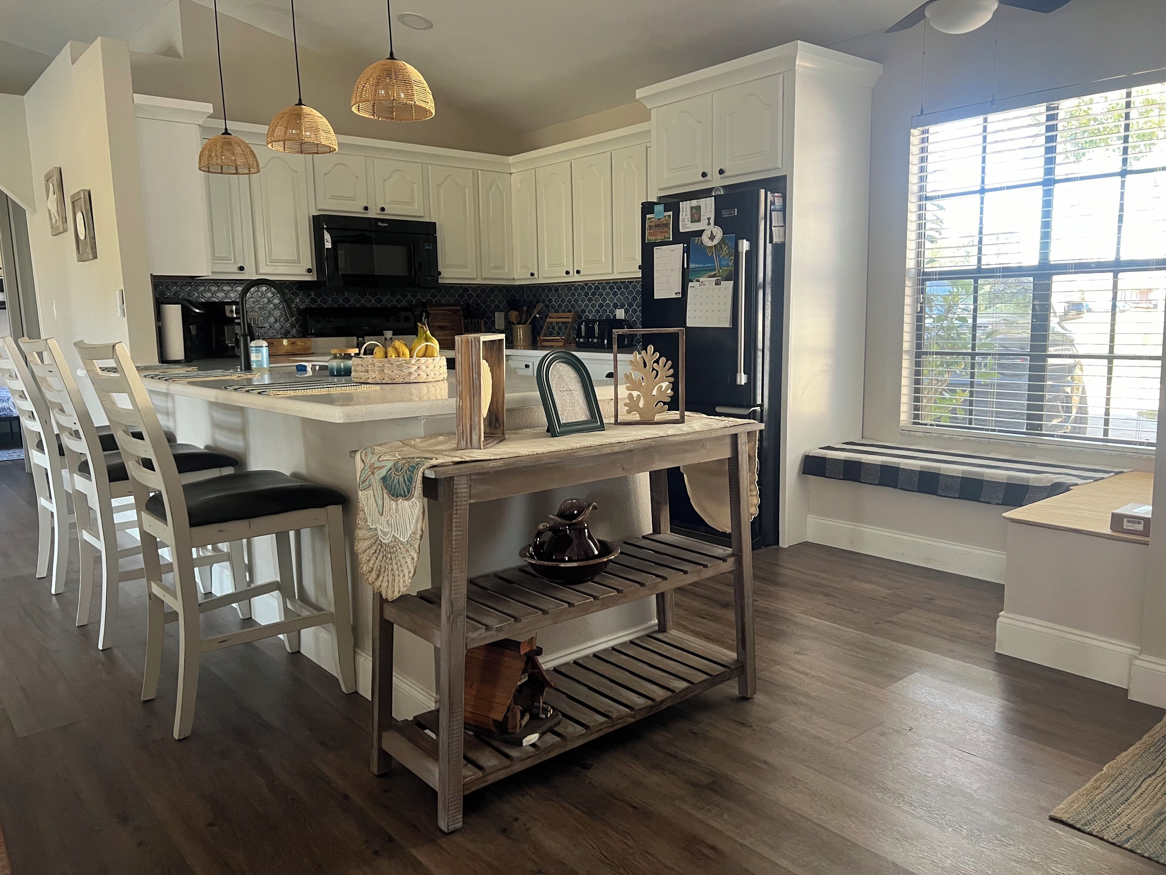 A modern kitchen with white cabinetry, a black refrigerator, and a dining area with wooden chairs and a table.