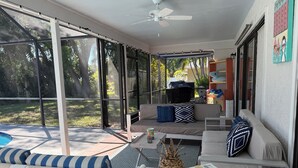 Une terrasse extérieure couverte, dotée d’un ventilateur de plafond, d’une table de billard et d’un coin salon avec des chaises et un canapé à rayures.