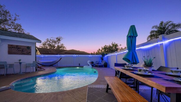 A pool area with a wooden deck, lounge chairs, and a dining table with umbrellas. - Tranquil Tropics| Heated Pool, Games, 10 to Beach (Largo)