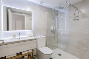 Un baño moderno con ducha de mampara de vidrio, lavamanos blanco y retrete.