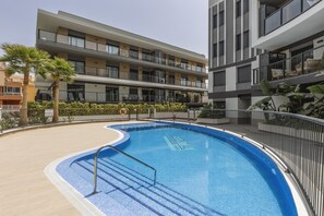 Un edificio moderno con piscina, balcones y un área ajardinada con palmeras.