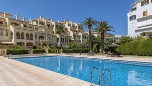 A swimming pool with a tiled deck, surrounded by a lush green hedge and palm trees. - Olive Beach (Javea / Xàbia)