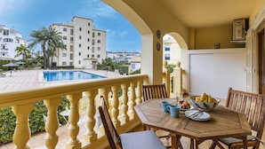 A balcony with a pool view, wooden furniture, and a bowl of fruit. - Olive Beach (Javea / Xàbia)